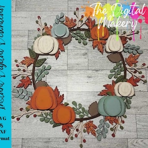 May include: A circular wreath design featuring layered wooden pumpkins in orange, white, and muted blue, accented with autumn leaves, sprigs, and berries. The text "The Digital Makery" and "Instant Digital Download SVG & DXF Format" is visible.
