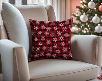 May include: Red and black plaid throw pillow with a white snowflake pattern. The pillow is on a white couch.
