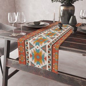 May include: A colorful table runner with a geometric pattern in shades of orange, blue, yellow, and white. The runner is made of fabric and has a fringed edge.