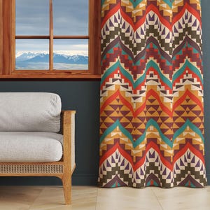 May include: A patterned curtain with a geometric design in shades of orange, red, brown, teal, and yellow. The curtain is hanging in a room with a wooden window and a grey sofa.