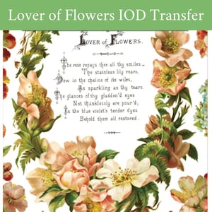 May include: A floral transfer with the text "Lover of Flowers IOD Transfer." The design features a central floral arrangement with light pink and yellow flowers, surrounded by a wreath of green leaves and additional blooms. A poem is also included.