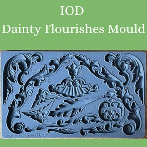 May include: A blue silicone mold with various decorative flourishes. The mold is labeled "IOD Dainty Flourishes IOD" and includes measurements in milliliters and grams.