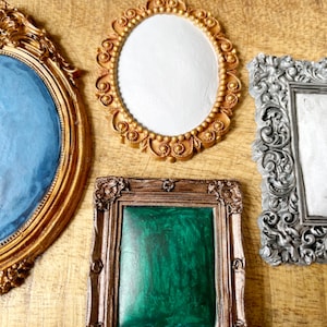 May include: Four ornate picture frames with different colored backgrounds. The frames are gold, silver, and bronze with intricate designs. The backgrounds are blue, white, green, and white.