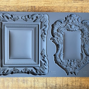 May include: A gray silicone mold with two ornate picture frame designs. The mold is labeled "Frames II IOD" and includes measurements in inches and ounces.