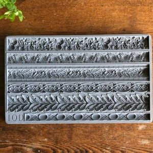 May include: A gray silicone mold with six different border designs. The mold is rectangular and has a textured surface. The mold is labeled "IOD".