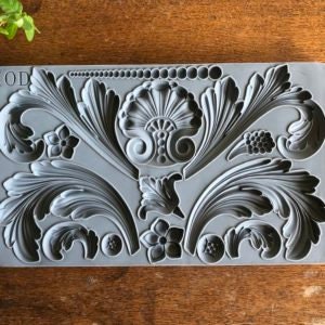 May include: A gray silicone mold with various decorative designs, including leaves, flowers, and swirls. The mold is designed for creating decorative elements for crafts and baking.
