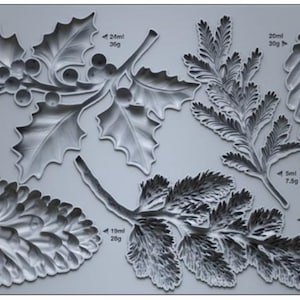 May include: A gray silicone mold featuring various winter foliage designs, including holly with berries, pine needles, and pine cones. The mold is labeled "IOD WINTER FORAGE" and includes measurements in milliliters and grams.