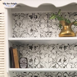 May include: White wooden shelf with two shelves, decorated with black and white patterned tile wallpaper. The top shelf has a gold pitcher with green leaves. The bottom shelf has two books and a small black and white sign that says "Faith will move mountains".
