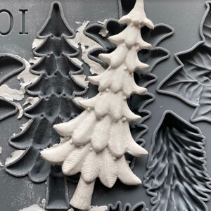 May include: A close-up of a silicone mold with various Christmas-themed designs. The mold features a tree, a poinsettia, and a leaf. The mold is gray and has a textured surface. The word "IOD" is printed on the mold.