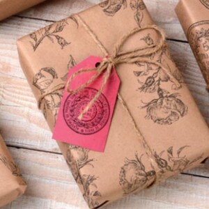 May include: Three brown paper gift packages wrapped with twine and decorated with red and pink paper tags. The packages are decorated with vintage illustrations of a deer, flowers, and coins.