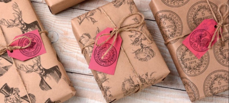 May include: Three brown paper gift packages wrapped with twine and decorated with red and pink paper tags. The packages are decorated with vintage illustrations of a deer, flowers, and coins.