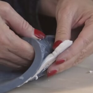 May include: A person's hands are shown pressing a white piece of clay into a gray silicone mold.