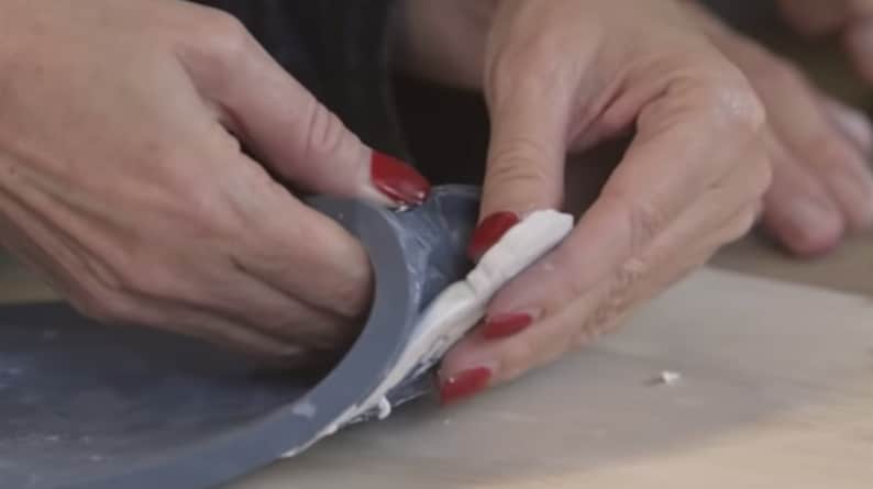 May include: A person's hands are shown pressing a white piece of clay into a gray silicone mold.