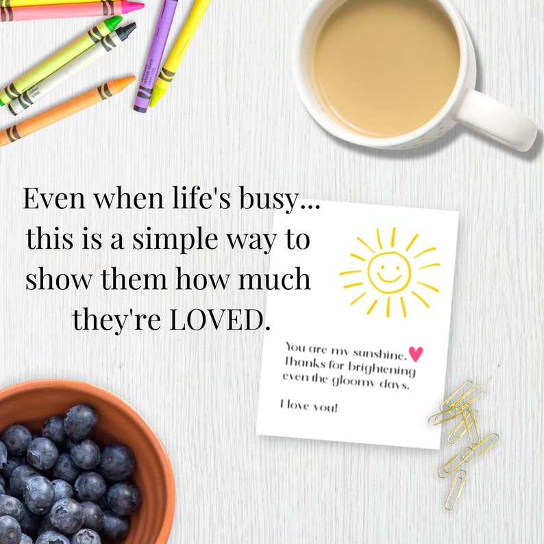 K&ouml;nnte beinhalten: Eine wei&szlig;e Karte mit einer gelben Sonne und dem Text "You are my sunshine. Thanks for brightening even the gloomy days. I love you!" Die Karte liegt auf einer wei&szlig;en Holzoberfl&auml;che mit einer Sch&uuml;ssel Blaubeeren, Buntstiften und einer Tasse Kaffee.