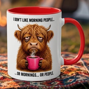 Peut inclure: Mug en céramique blanche avec intérieur et anse rouges. L'illustration représente une vache des Highlands tenant une tasse rose de café, avec le texte "I DON'T LIKE MORNING PEOPLE... ...OR MORNINGS... OR PEOPLE."