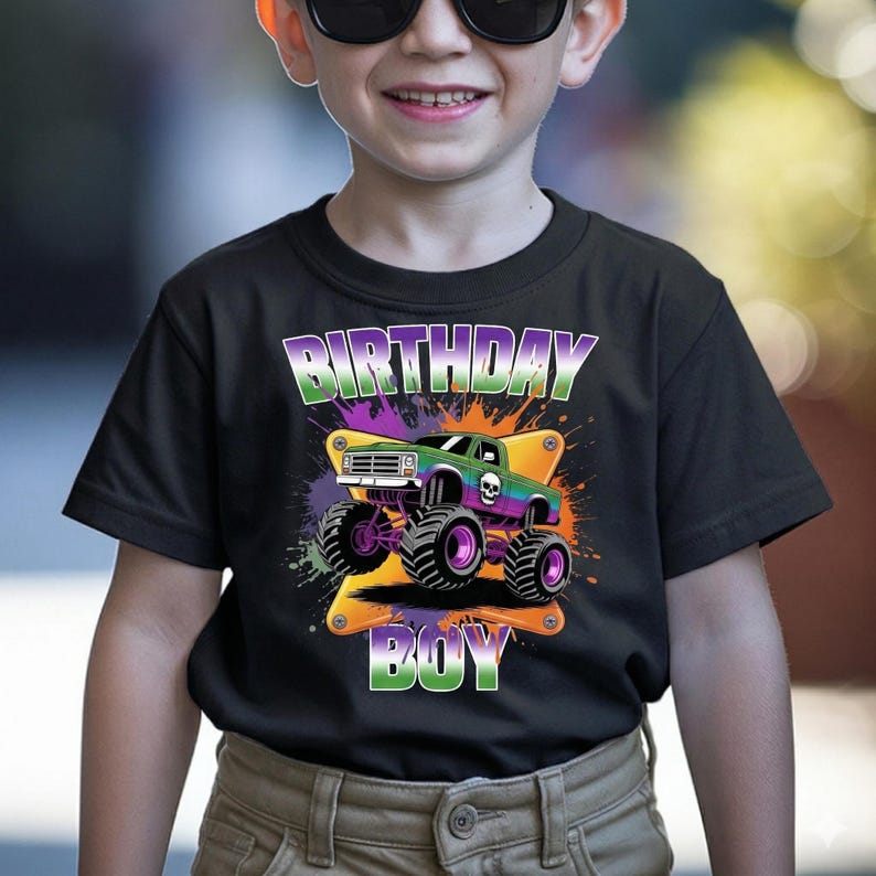 May include: Black t-shirt featuring a monster truck graphic with the text "BIRTHDAY BOY". The truck is green and purple with large black and purple tyres. The design includes colourful splashes.