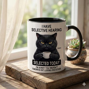 Peut inclure: Une tasse en céramique blanche avec une anse noire et le texte "But First, Coffee" en gras noir. La tasse est posée sur un fond flou, suggérant un cadre chaleureux.