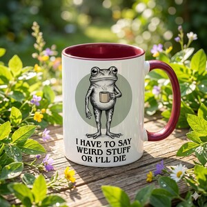 Peut inclure: Mug en céramique blanche avec intérieur et anse bordeaux. La tasse présente une grenouille de dessin animé tenant une tasse à café, sur un cercle vert. Le texte sur la tasse se lit : "I HAVE TO SAY WEIRD STUFF OR I'LL DIE."