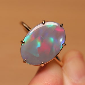 May include: A silver ring with a large oval opal gemstone. The opal has a white base with iridescent flashes of blue, green, and pink.