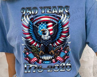 May include: Blue jean-colored t-shirt with a graphic of a bald eagle, American flag, and the text "250 YEARS 1776-2026." The eagle has red, white, and blue wings. The shirt is made of a soft material and has short sleeves.