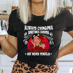 May include: Black t-shirt with a graphic of a woman with red flowers and the text "Always Chingona Sometimes Carrrona - But Never Pendeja -"