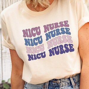 May include: A white t-shirt with the text "NICU NURSE" repeated four times in a retro font. The text is in shades of purple and blue.