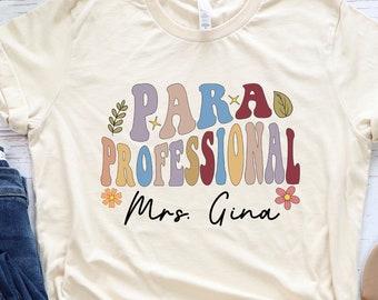 May include: A beige t-shirt with the text "Para-Professional Mrs. Gina" in a retro font with colorful letters and floral accents.