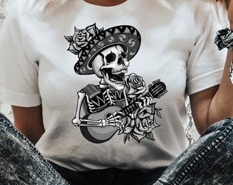 May include: A white t-shirt with a black and white illustration of a skeleton playing a guitar. The skeleton is wearing a sombrero and has a rose in its hand.