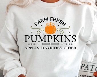 Könnte beinhalten: Weißer Pullover mit einem schwarzen grafischen Design, auf dem "Farm Fresh Pumpkins Apples Hayrides Cider" steht. Die Grafik zeigt einen stilisierten Kürbis mit Stiel und Blättern.