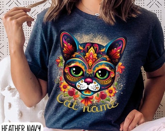 May include: Heather navy blue t-shirt with a colorful sugar skull cat design and the text "Cat name".