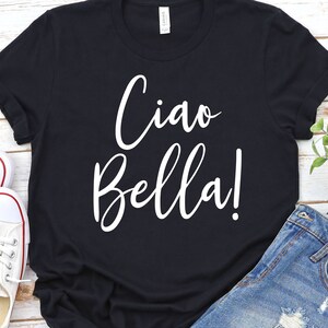 K&ouml;nnte beinhalten: Schwarzes T-Shirt mit dem Schriftzug "Ciao Bella!" in wei&szlig;er Schrift. Das Shirt wird mit blauen Jeansshorts und wei&szlig;en Turnschuhen kombiniert. Ein l&auml;ssiges und stilvolles Outfit.