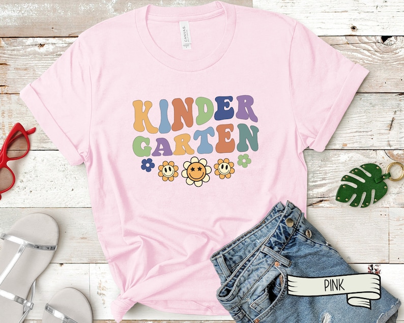 Puede incluir: Camiseta rosa con el texto "KINDERGARTEN" en colores arco&iacute;ris y un dise&ntilde;o floral. La camiseta est&aacute; hecha de un material suave y c&oacute;modo.