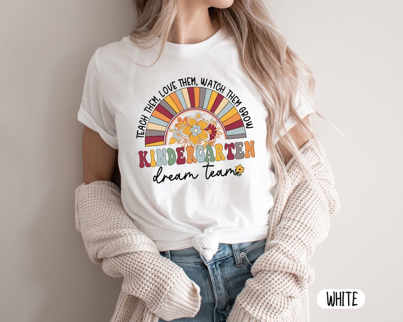 May include: White t-shirt with a rainbow and flower design. The text "Teach them, love them, watch them grow, Kindergarten dream team" is printed on the shirt.