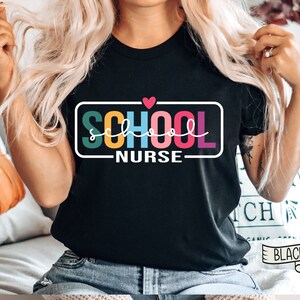 May include: A black t-shirt with a rainbow colored "SCHOOL NURSE" graphic and a small red heart above the text.