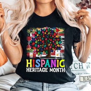 May include: Black t-shirt with a colorful tree made of handprints and the text "Hispanic Heritage Month". The tree is surrounded by a flag with different colors and designs.