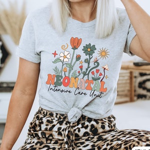 May include: Grey t-shirt with a floral design and the text "Neonatal Intensive Care Unit" in colorful letters.