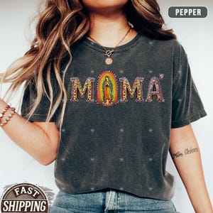 May include: A gray t-shirt with the word "MOMA" in rhinestones. The "O" is a depiction of the Virgin Mary.