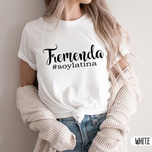 May include: White t-shirt with the text "Tremenda #soylatina" in black cursive lettering.