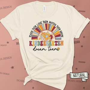 May include: A beige t-shirt with a rainbow and floral design. The text "Teach them, love them, watch them grow" is written in a circle around the rainbow. The text "Kindergarten dream team" is written below the rainbow.