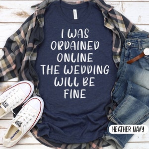 May include: A heather navy blue t-shirt with the text "I was ordained online the wedding will be fine" in white lettering.