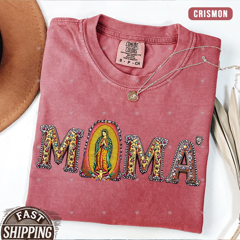 May include: A red t-shirt with the word "MOMA" in colorful letters with floral designs. The letter "O" features a depiction of the Virgin Mary in a gold frame.
