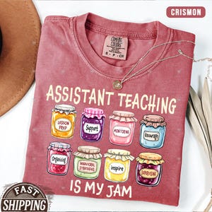 Puede incluir: Una camiseta roja con el texto "Assistant Teaching is my jam" y un gr&aacute;fico de tarros de mermelada con palabras como "Lesson Prep", "Support", "Monitoring", "Encourage", "Organizing", "Behavioral Strategies", "Inspire" y "Supervising" en ellos.