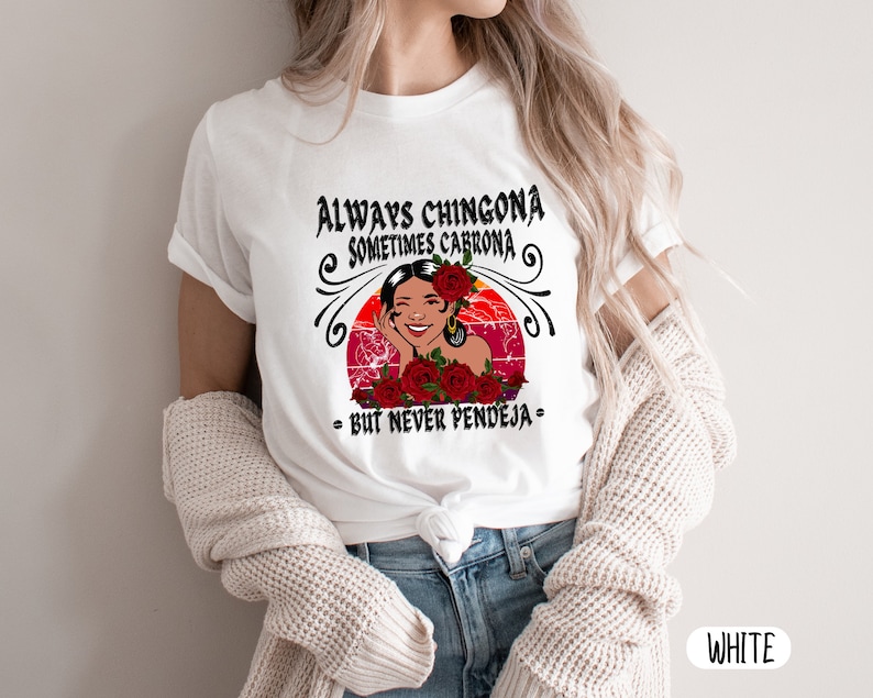 May include: White t-shirt with a graphic design featuring a woman with red flowers and the text "Always Chingona Sometimes Cabrona - But Never Pendeja -"