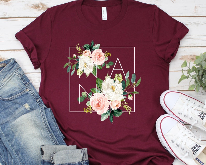 May include: Burgundy t-shirt with a white square frame around a floral design that spells out "NANA".