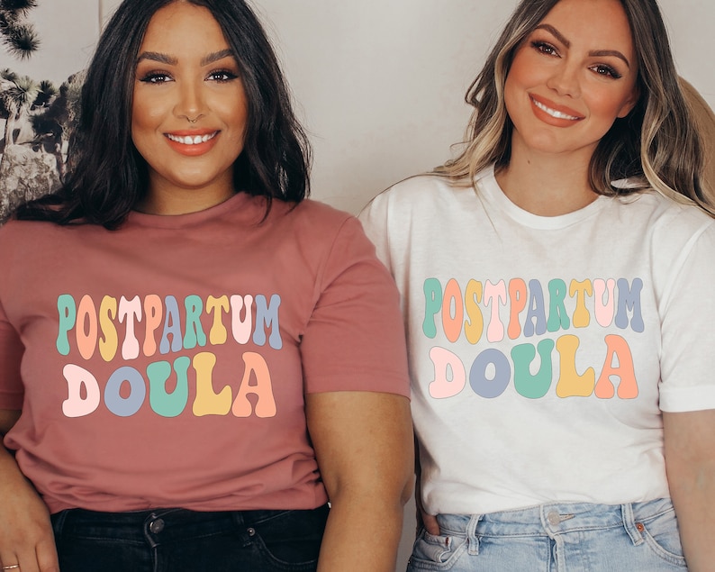 May include: Two women wearing t-shirts with the text "POSTPARTUM DOULA" in colorful retro font. The shirts are pink and white.