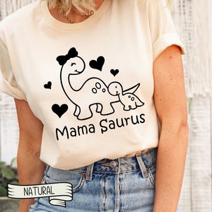May include: A white t-shirt with a black graphic of a dinosaur mom and baby dinosaur with hearts and the text "Mama Saurus".