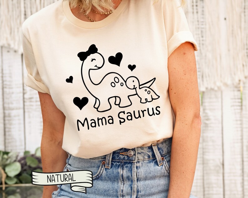 May include: A white t-shirt with a black graphic of a dinosaur mom and baby dinosaur with hearts and the text "Mama Saurus".