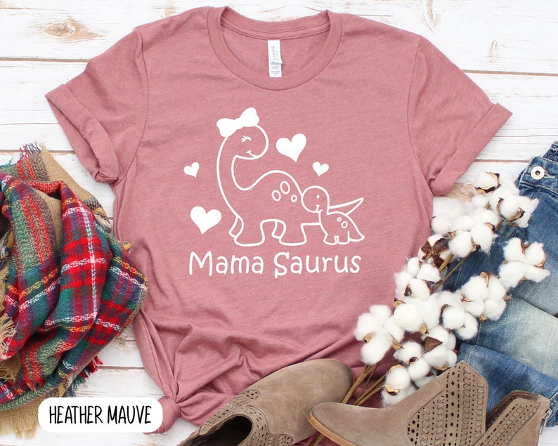 May include: Heather mauve t-shirt with a white graphic of two dinosaurs with hearts and the text "Mama Saurus".