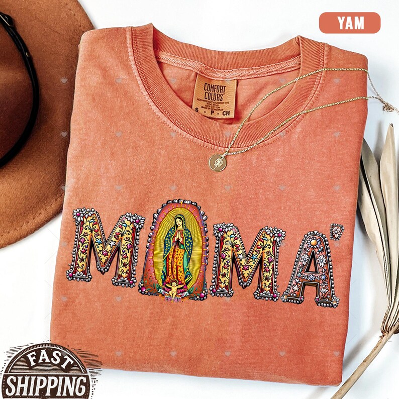 May include: A peach-colored t-shirt with the word "MOMA" printed in colorful letters with floral designs. The letter "O" features an image of the Virgin Mary.