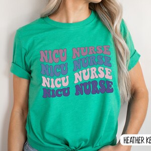 May include: A green t-shirt with the text "NICU NURSE" repeated four times in a retro font. Each word is a different color: pink, purple, blue, and light purple.